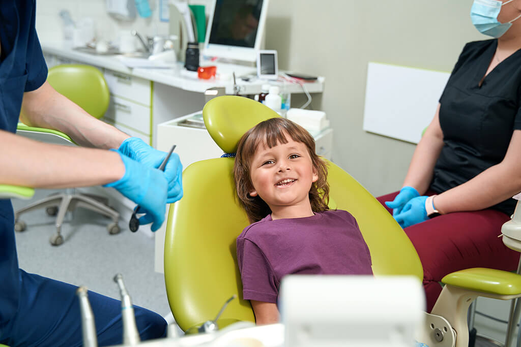 Cheerful little patient is sitting in pedodontist office before examinatio